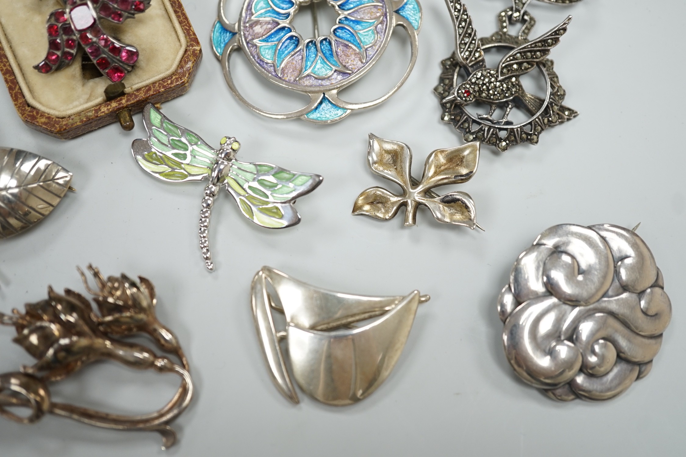 An early 20th century white metal and foil backed garnet cluster set bird brooch, 27mm and eight other assorted mainly 925 brooches including two enamelled and one Finnish yacht brooch.
